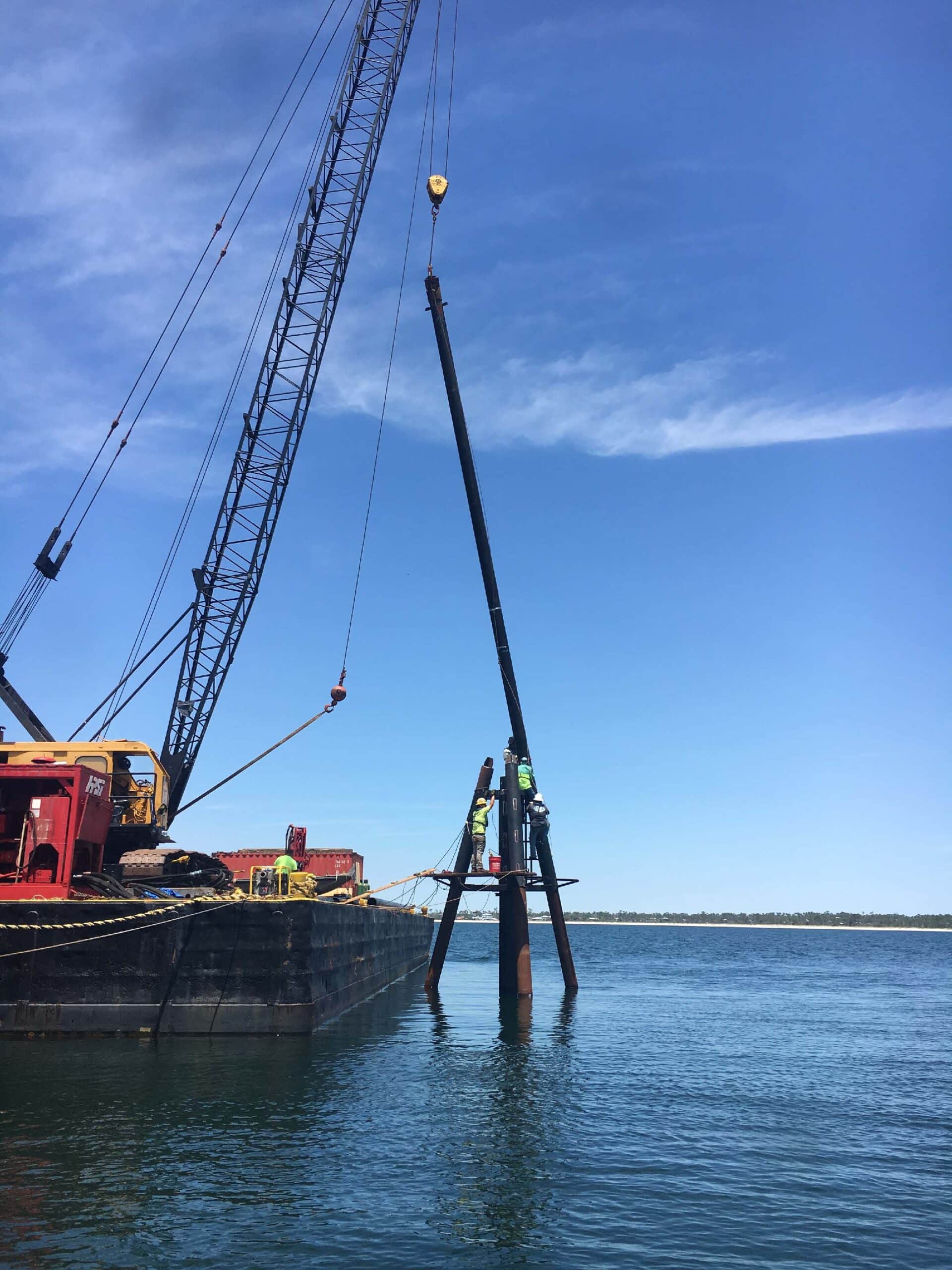 Marine construction project in progress , pole being installed in water with equipment in tow | Inland Construction & Engineering, Inc. Panama City, Florida providing construction, general contracting, marine construction, design & engineering, diving services, roofing, & bulding rehab.